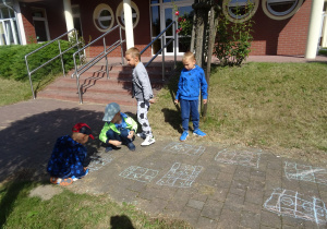 dzieci całą grupa malują kredą wzorki na chodniku